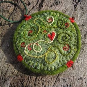 Runder grüner Filzanhänger mit spiralförmiger Stickerei in Rot und Creme sowie gesticktem Herz – gefilzt von Corinna Nitschmann